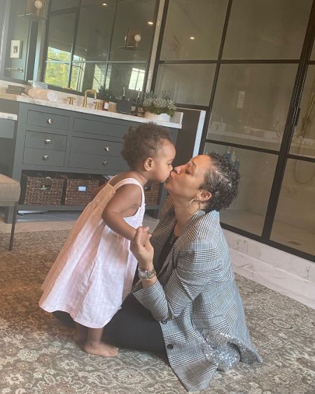 Tia Mowry in a grey sweater kisses her daughter.
